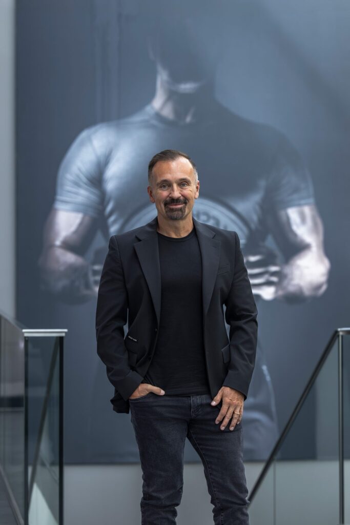 Gottfried Wurpes steht lächelnd vor einem großen Fitness Plakat